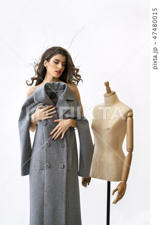 Model covers her body with gray coat near sewing mannequin 47480015