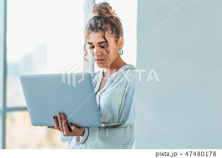 Attractive businesswoman standing on a waterfront promenade working on a laptop computer as she Attractive businesswoman standing on a waterfront promenade working on a laptop computer as she 47480178