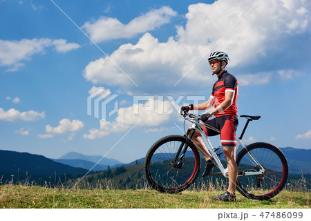 Sportsman cyclist standing with cross country bike, enjoying beautiful view of distant mountains Sportsman cyclist standing with cross country bike, enjoying beautiful view of distant mountains 47486099