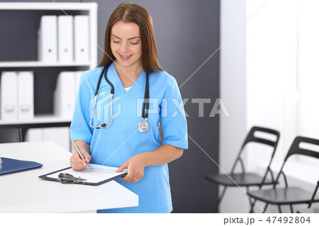 Doctor woman at work. Portrait of female physician filling up medical form while standing near Doctor woman at work. Portrait of female physician filling up medical form while standing near 47492804