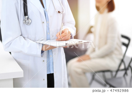 Doctor woman filling up medical form while standing near reception desk at clinic or emergency Doctor woman filling up medical form while standing near reception desk at clinic or emergency 47492986