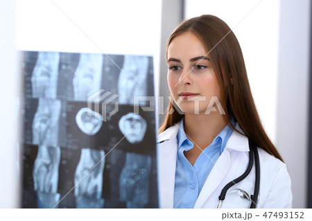 Doctor woman examining x-ray picture while standing near window in hospital. Surgeon or orthopedist Doctor woman examining x-ray picture while standing near window in hospital. Surgeon or orthopedist 47493152