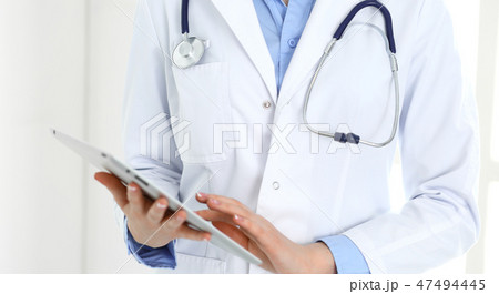 Woman doctor using tablet computer while standing straight in hospital closeup. Healthcare 47494445