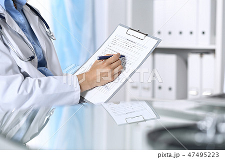 Female doctor filling up medical form on clipboard, closeup. Reflecting glass table is a physician Female doctor filling up medical form on clipboard, closeup. Reflecting glass table is a physician 47495223