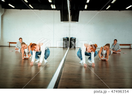 Red-haired ballet teacher in blue jeans showing movements to her students Red-haired ballet teacher in blue jeans showing movements to her students 47496354