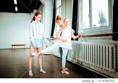 Long-haired blond teenager in white sport clothing exercising near the ballet bar 47496502