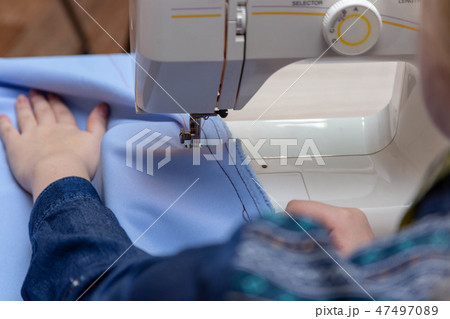 Close-up sewing machine, needle sews. The hand of a girl seamstress holds fabric 47497089