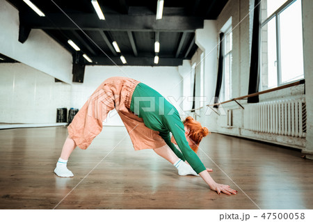 Beautiful slim yoga coach in a green turtleneck stretching her back Beautiful slim yoga coach in a green turtleneck stretching her back 47500058