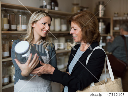 A female shop assistant serving a senior customer in a zero-waste shop. A female shop assistant serving a senior customer in a zero-waste shop. 47512103