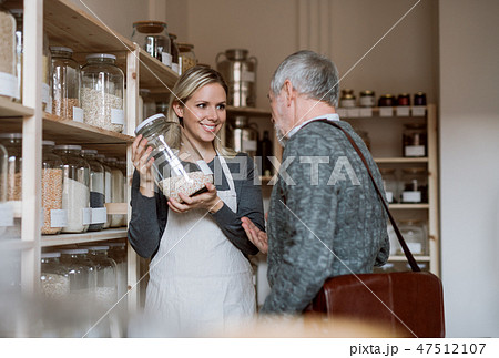 Young female shop assistant serving a senior man in a zero waste shop. Young female shop assistant serving a senior man in a zero waste shop. 47512107