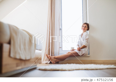 A young woman with night shirt sitting by the window in the morning. 47512156