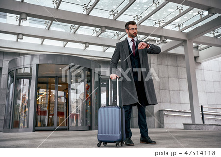 Young man checking his watch and pulling suitcase 47514118