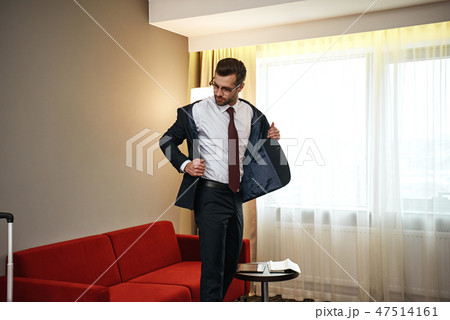 Business man with suitcase takes off his jacket near sofa at hotel room Business man with suitcase takes off his jacket near sofa at hotel room 47514161