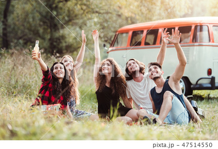 A group of young friends with drinks sitting on grass on a roadtrip through countryside. A group of young friends with drinks sitting on grass on a roadtrip through countryside. 47514550