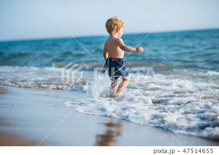 A small toddler boy with shorts walking in water on beach on summer holiday. 47514655