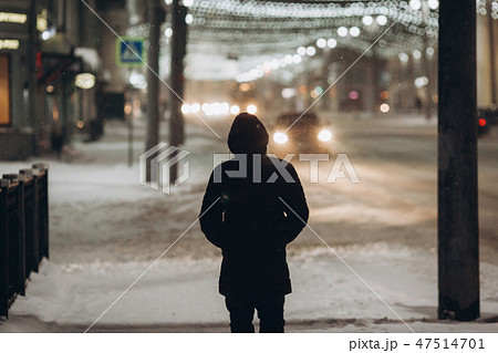 Silhouette of a man in the hood that walks down the street at night in the snowfall 47514701
