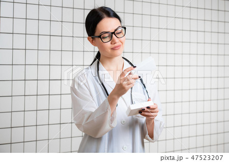 A friendly cute girl with dark hair and glasses, wearing a lab coat, reads carefully the information A friendly cute girl with dark hair and glasses, wearing a lab coat, reads carefully the information 47523207