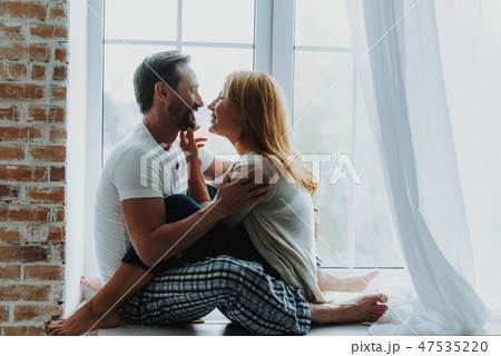 Beloved couple tenderly hugging on window sill Beloved couple tenderly hugging on window sill 47535220