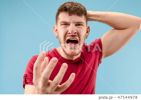 The young emotional angry man screaming on blue studio background The young emotional angry man screaming on blue studio background 47544978