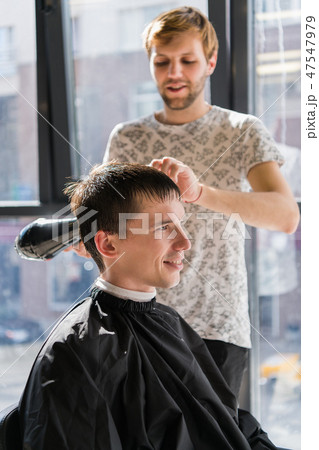 Barber with hairdryer drying and styling hair of client. Styling concept 47547979