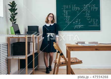 Sad schoolgirl standing in front of blackboard. 47554268