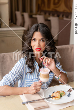 Beautiful young woman enjoying coffee cappuccino or latte in a glass cup with foam. Light breakfast Beautiful young woman enjoying coffee cappuccino or latte in a glass cup with foam. Light breakfast 47560459