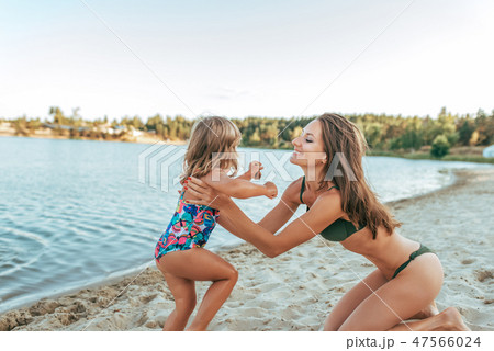 Beautiful young woman mom playing on shore of the lake with sand, holding a small child daughter 47566024