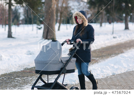 Beautiful mother walking in the park with her little baby in stoller. Woman dressed in blue jaket 47567024