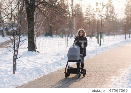 Beautiful mother walking in the park with her little baby in stoller. Woman dressed in blue jaket Beautiful mother walking in the park with her little baby in stoller. Woman dressed in blue jaket 47567066