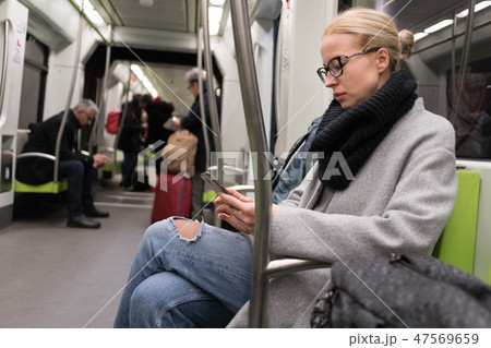 Beautiful blonde woman wearing winter coat and scarf reading on the phone while traveling by metro 47569659