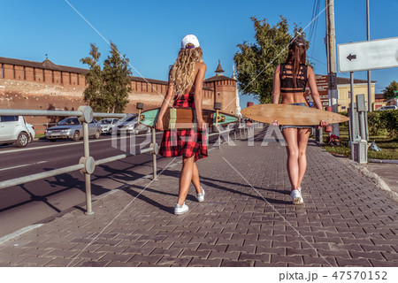Two girls walking on foot, women girlfriends in summer in the city on the road. With a longboard 47570152