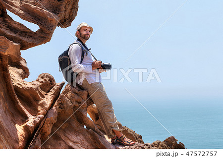 Traveller with camera sits on the edge of a cliff. 47572757