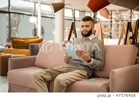 Serious concentrated man sitting on sofa and reading brochure 47576408