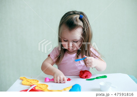 Child girl sitting at table playing with clay 47591816