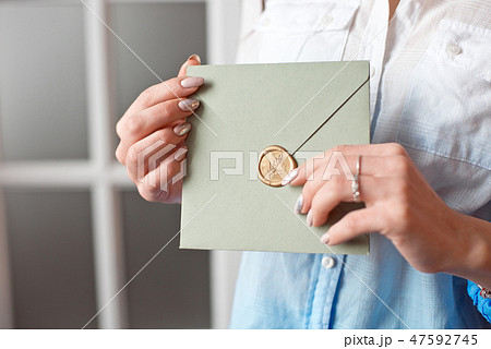Close-up woman with slim body holding in hands the invitation card gray-green color square shape 47592745