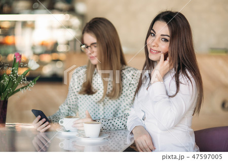 Two girls sitting in a cafe drinking cappuccino and using smartphone. Modern girl Two girls sitting in a cafe drinking cappuccino and using smartphone. Modern girl 47597005