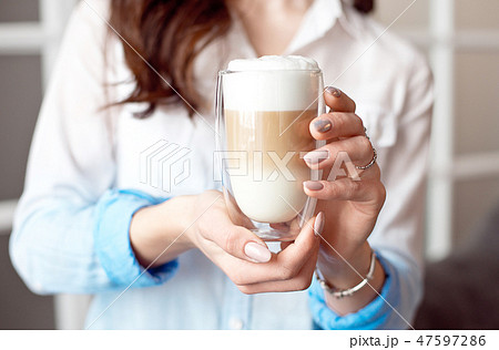 Close-up of female hands in office clothes holding a glass cup of coffee with soy milk during a Close-up of female hands in office clothes holding a glass cup of coffee with soy milk during a 47597286