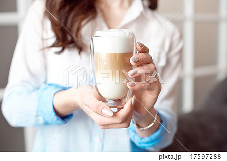 Close-up of female hands in office clothes holding a glass cup of coffee with soy milk during a Close-up of female hands in office clothes holding a glass cup of coffee with soy milk during a 47597288