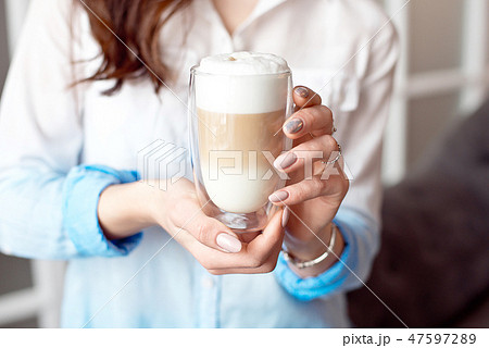 Close-up of female hands in office clothes holding a glass cup of coffee with soy milk during a 47597289