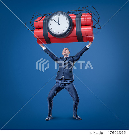 A joyful businessman in smart suit holding up a huge bundle of dynamite with a time bomb attached to A joyful businessman in smart suit holding up a huge bundle of dynamite with a time bomb attached to 47601346