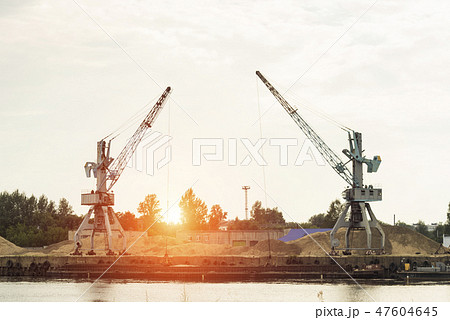 Two port cranes at the riverbank produce river sand, sunset, barge 47604645