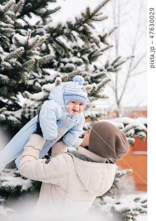 Mom near the snow covered Christmas tree plays with the bab Mom near the snow covered Christmas tree plays with the bab 47630029