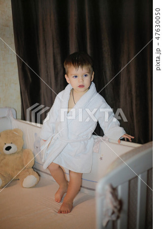 A little boy stands on the bed and poses in a home robe A little boy stands on the bed and poses in a home robe 47630050