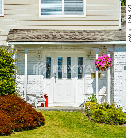Entrance of the house with backet of flowers, two white chairs, and red churn 47634498