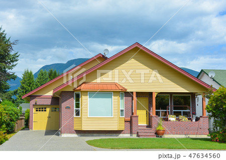 Yellow residential house with accurate lawn and concrete driveway to the garage 47634560