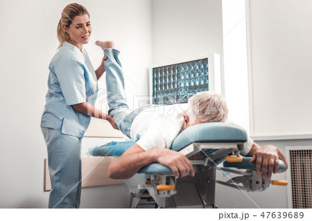Chiropractor in blue uniform checking legs of elderly man 47639689