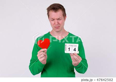 Sad young man holding calendar block and heart ready for Valentine's day 47642502
