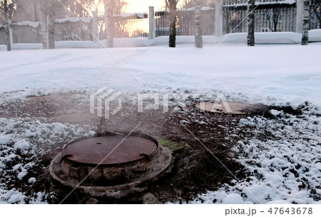 Close-up steam is from sanitary sewer cover in snow in winter park. Melted snow around. Close-up steam is from sanitary sewer cover in snow in winter park. Melted snow around. 47643678