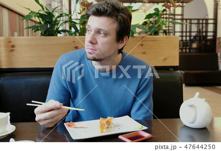 The young man brunette eats roll by wood sticks. Front view. The young man brunette eats roll by wood sticks. Front view. 47644250