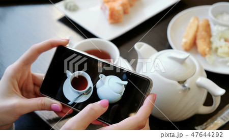 Woman's hands leafing through photos of cups of tea and teapot on the screen of the mobile phone. 47644292